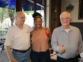 Smiling diverse group of three people posing indoors, one man giving thumbs up, friendly and casual atmosphere