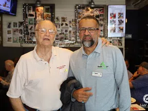 Two men posing and smiling in a casual restaurant setting with photo-covered walls in the background.