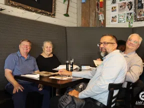 Four diverse adults smiling and sitting around a table at a cozy restaurant with menus and drinks.