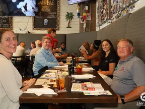Group of people smiling and seated around a long table in a casual seafood restaurant with menus and drinks.