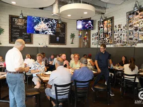 Crowded seafood restaurant interior with diners, wall menus, TVs, and photos on rustic wooden walls.