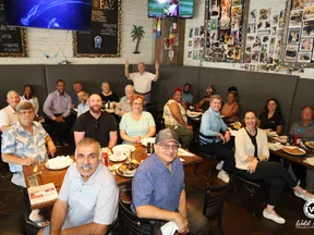 Group of diverse adults enjoying a meal together in a cozy restaurant with photos on the walls and TV screens.