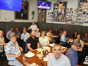 Group of diverse people smiling and sitting around tables at a casual restaurant with food and drinks