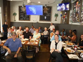 Group of diverse adults sitting and smiling in a casual restaurant with seafood menu and TV screens