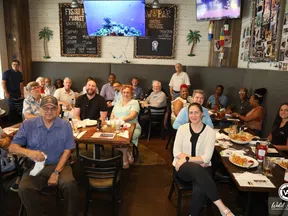 Group of diverse people enjoying a meal together at a casual seafood restaurant with menus and TVs on walls.