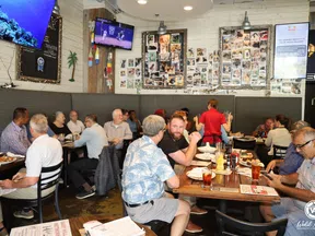 Busy restaurant scene with diverse patrons dining, watching TV, and chatting in a casual, lively atmosphere.