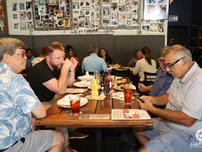 Group of men sitting and dining at a wooden table in a casual restaurant with wall photos in background.