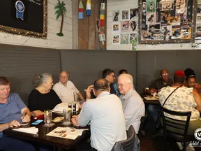 Group of people dining and conversing in a cozy restaurant with dog photos on the wall and string lights.