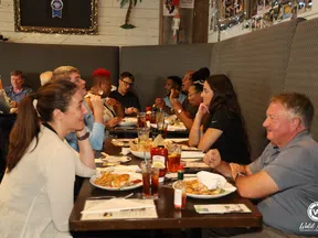 Group of people enjoying a meal and conversation at a long restaurant table with various dishes and drinks.