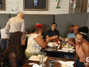 Diverse group of people dining and conversing at a restaurant table with drinks and menus.