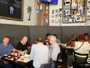 Group of diverse people dining and conversing in a cozy restaurant booth with decorated walls.