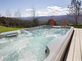 Outdoor hot tub with bubbling water on wooden deck overlooking trees and distant mountains under blue sky.