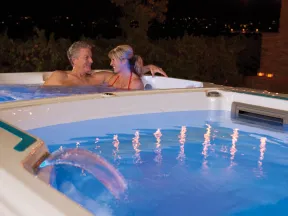 Couple relaxing together in a hot tub with water jets and night city lights in the background.