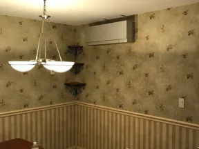 Dining area with floral and striped wallpaper, chandelier light fixture, air conditioner, and wooden table.