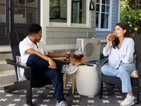 Couple relaxing on patio chairs, enjoying iced tea together on a sunny day outside a modern home.