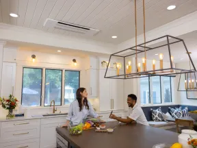 Couple enjoying conversation in a modern white kitchen with large island and pendant lights.