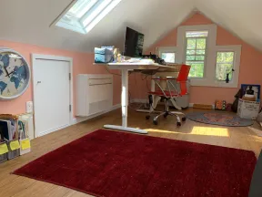 Bright attic home office with pink walls, skylight, red chair, white desk, and large red rug on wood floor.