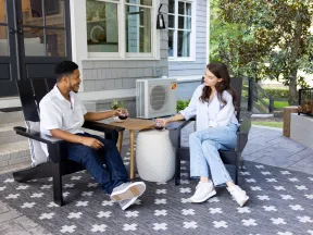 Two people relaxing and chatting on a patio with drinks, seated on black chairs over a patterned rug.