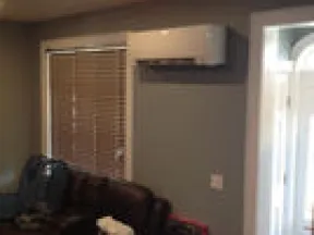 Living room with dark leather sofa, wall-mounted air conditioner, and window blinds on gray walls.