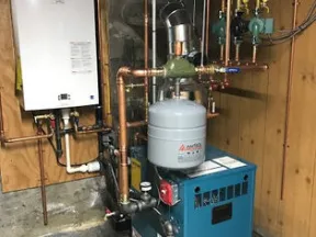 Basement heating system with a blue boiler unit, white wall-mounted heater, and copper piping setup.