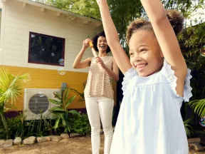 Happy mother and daughter playing with bubbles outdoors in a sunny backyard garden.