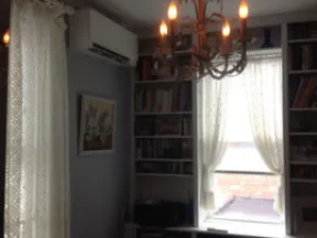 Cozy room with lace curtains, bookshelf, chandelier lighting, and air conditioning unit on the wall.