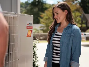 Woman smiling while inspecting a Mitsubishi Electric Smart Multi outdoor unit on a sunny day.
