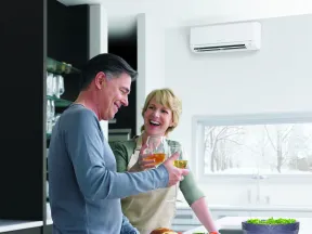 Middle-aged couple in kitchen enjoying wine, preparing fresh salad with bread and tomatoes on counter.
