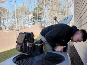 Technician inspecting a residential Rheem air conditioning unit outside a house on a sunny day.