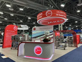 Oakes trade show booth with red and white branding celebrating 79 years, featuring industrial machines and display screens.