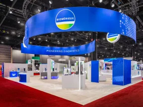Exhibition booth with blue circular overhead banner displaying Biomérieux logo and pioneering diagnostics message
