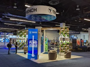 Trade show booth for Trench featuring modern design, digital displays, and seating area with greenery