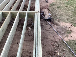 Wooden deck frame construction in progress on a backyard with grass and a walkway visible.