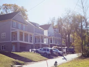 Newly constructed two-story townhouses with front porches on a sunny residential street with parked vehicles.
