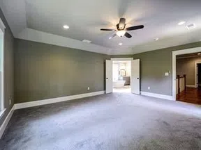 Spacious empty bedroom with gray carpet, green walls, ceiling fan, and double doors leading to a bathroom.