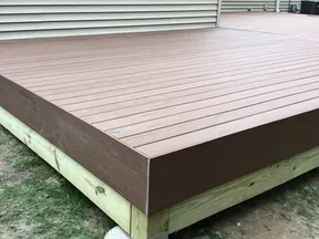 Newly constructed wooden deck with composite brown decking boards next to a beige house exterior.