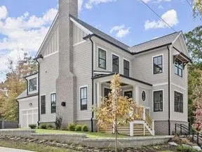 Modern two-story white house with black trim, large chimney, front porch, and landscaped yard in autumn.