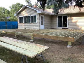 Wooden deck frame under construction attached to beige house with windows and door in backyard.