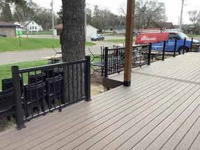 Spacious wooden deck with black metal railing, tree, and a red Mr. Handyman van parked on the street nearby.