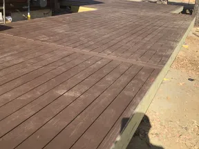 Newly constructed elevated wooden deck attached to a log cabin with nearby parking and trees.