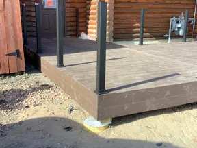 Newly constructed brown wooden deck with black metal posts attached to a log cabin exterior door.