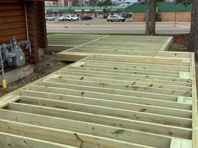 Close-up of wooden deck framing attached to log cabin exterior under cloudy sky with street and buildings in background