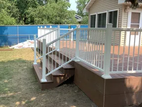 Backyard wooden deck with white railing and steps attached to beige house under trees.
