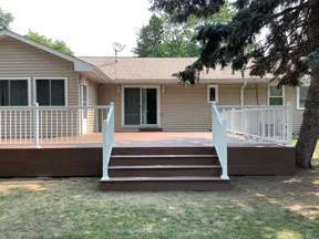 Backyard wooden deck with white railing and stairs attached to beige house with sliding glass door.