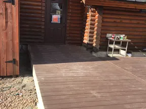 Newly built raised wooden deck attached to a rustic log cabin with a metal roof and a dark door.