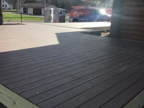 Newly constructed two-tone wood deck outside a log cabin with a handyman service van in the background.