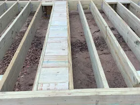 Wooden floor joists and beams laid out for deck construction next to a log cabin exterior door.