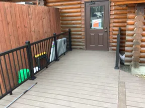 Spacious wooden deck with black metal railing leading to a brown door on a log cabin exterior.