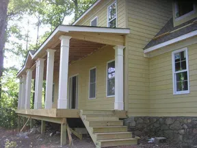 Yellow house under construction with stone foundation and wooden porch supported by white columns
