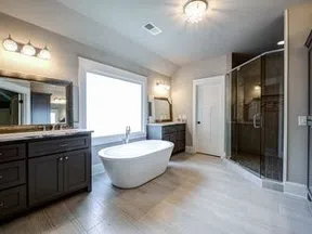 Modern bathroom with freestanding tub, dual vanities, large window, and glass-enclosed shower with tiled floor.